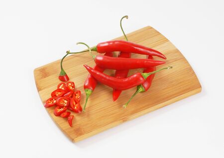 whole and sliced chili peppers on wooden cutting boardの写真素材