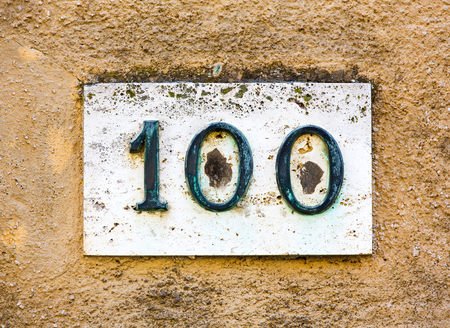 Rusty metal house number 100 on a weathered wallの写真素材