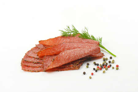 Thin slices of black pepper salami with peppercorns on white backgroundの写真素材
