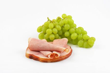 stack of ham slices and bunch of white grapes on white backgroundの写真素材