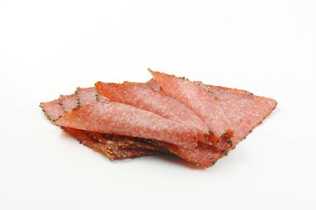 Thin slices of pepper coated salami on white backgroundの写真素材