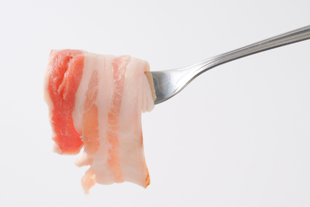 Thin slice of fresh side bacon on a forkの写真素材