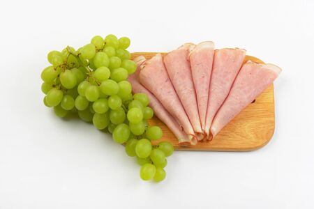 slices of ham and bunch of white grapes on wooden cutting boardの写真素材