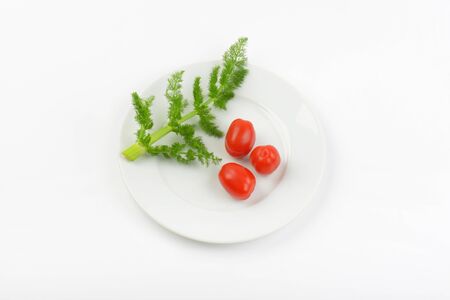 twig of dill and cherry tomatoes on white plateの写真素材