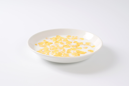 plate of corn flakes with fresh milk on off-white background with shadows