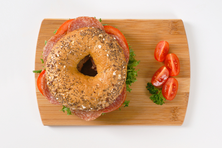 bagel sandwich with salami on wooden cutting boardの写真素材