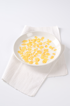 plate of corn flakes with fresh milk on white place mat