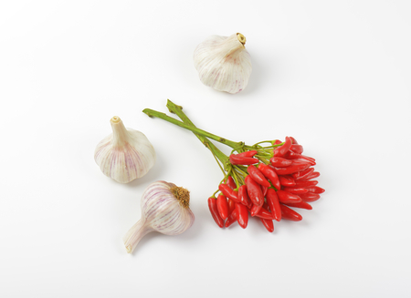 Bunch of small red chili peppers and garlic bulbs on white background