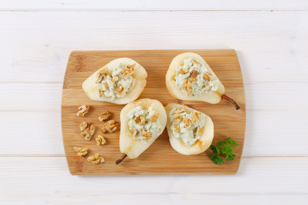 halved pears with blue cheese and walnuts on wooden cutting boardの写真素材