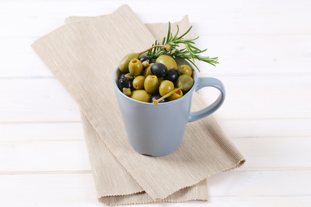 cup of pickled olives, capers and caper berries on beige place matの写真素材