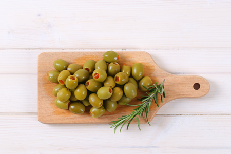 pile of green olives stuffed with red pepper on wooden cutting boardの写真素材