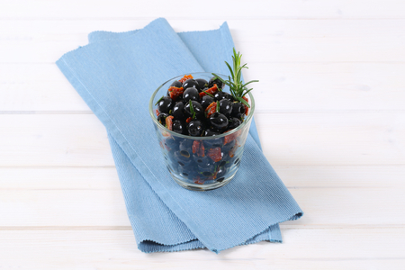 glass of black olives with dried tomatoes on blue place matの写真素材