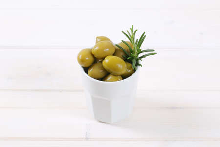 cup of green olives with fresh rosemary on white backgroundの写真素材