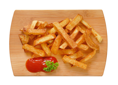 heap of fried chipped potatoes with ketchup on wooden cutting board