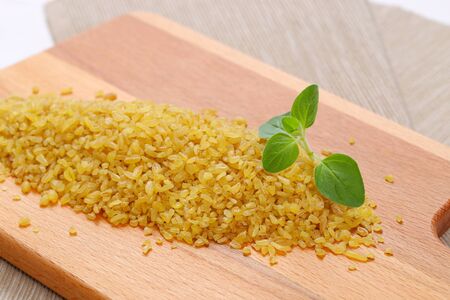 pile of dry wheat bulgur on wooden cutting board - close upの写真素材