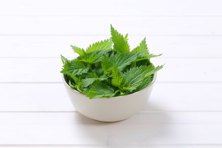 bowl of fresh nettle leaves on white wooden backgroundの写真素材