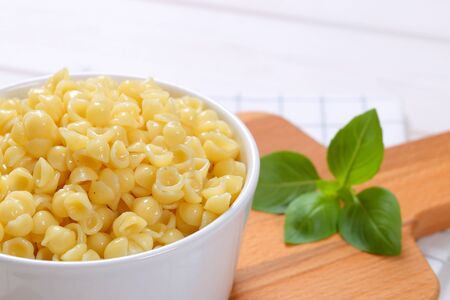 bowl of small pasta shells on wooden cutting board - close upの写真素材