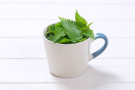 mug of fresh nettle leaves on white wooden backgroundの写真素材