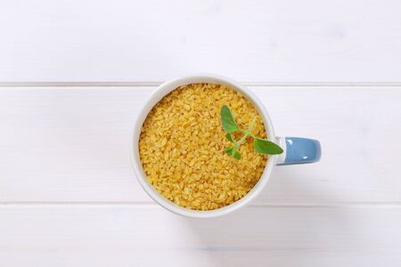 mug of dry wheat bulgur on white wooden backgroundの写真素材