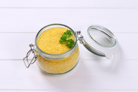 jar of raw millet on white wooden backgroundの写真素材