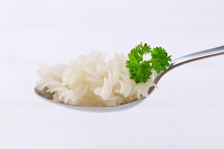 spoon of cooked rice pasta fusilli on white wooden backgroundの写真素材