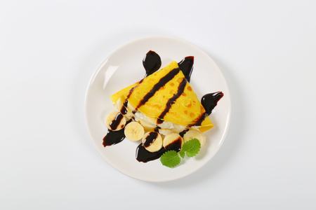 Crepes with slices of banana, whipped cream and chocolate sauceの写真素材