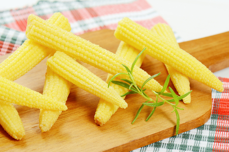 stack of sweet baby corn on wooden cutting board - close upの写真素材