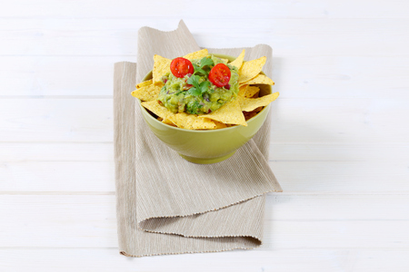 bowl of corn tortilla chips with guacamole dip on beige place matの写真素材