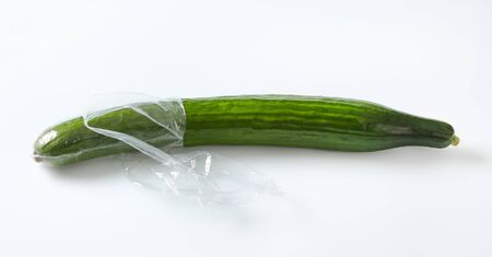 single long cucumber unwrapped and unpeeled on white backgroundの写真素材