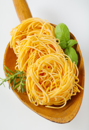 bundles of spaghetti pasta and herbs in wooden scoopの写真素材