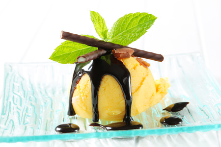 Scoop of yellow ice cream topped with chocolate sauce and mint sticksの写真素材