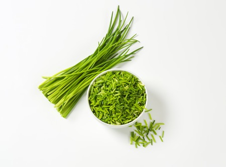 Bowl of fresh chopped chives and bundle of chives next to itの写真素材