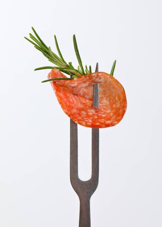 Slice of Hungarian salami and fresh rosemary on forkの写真素材
