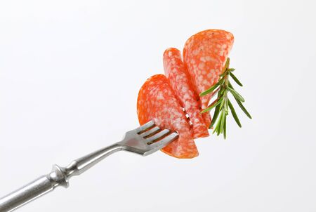 Slices of Hungarian salami and fresh rosemary on forkの写真素材