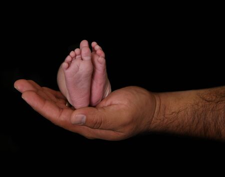 Father holding his newborn infant's feet on blackの写真素材