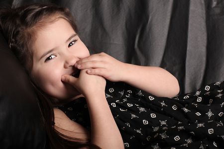 Young Child Giggling on the Couch With Hand Over Her Mouthの写真素材