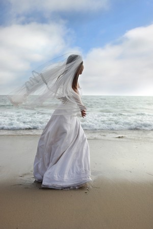 Bride Walking Along the Beach with her Veil Blowing in the Windの写真素材