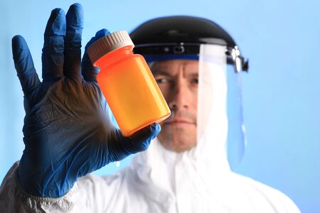 Male Lab Technician Wearing Protective Gear Holding Medication Bottle
