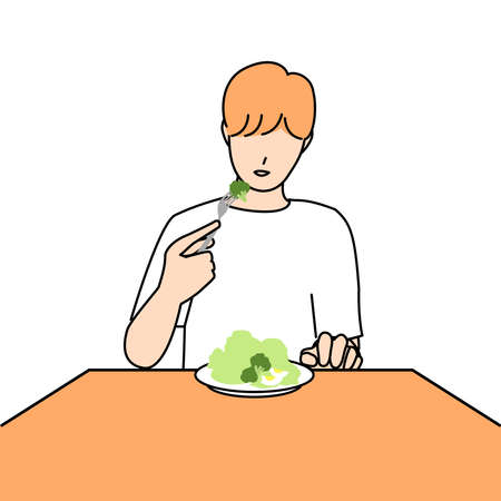 A young man with orange hair is eating a salad.の写真素材