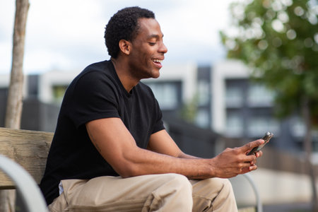 Happy man sitting on a wooden bench, holding a smartphoneの写真素材