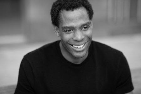 Black and white close-up portrait of a man smiling and looking down, sitting outdoorsの写真素材