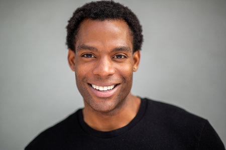 Close-up portrait of a man smiling directly at the camera, set against a plain gray backgroundの写真素材