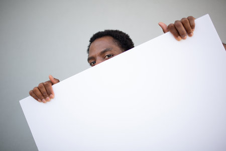 A man holding a large blank white signboard, partially hiding his face behind itの写真素材