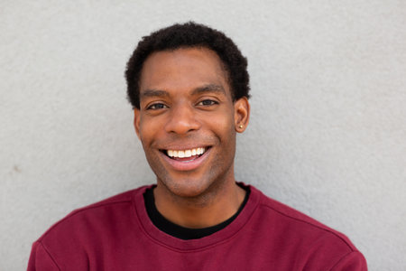 A close-up portrait of a man smiling in a red sweater, standing in front of a grey backgroundの写真素材