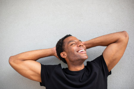 Portrait of a man smiling with his hands behind his head, eyes closed, against a plain gray backgroundの写真素材