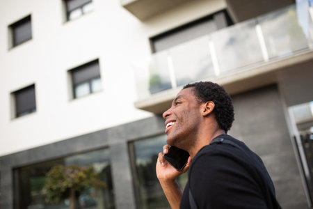 Side view of a man in a black t-shirt smiling while holding a smartphone to his earの写真素材