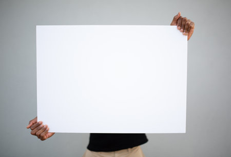 A man holding a large blank white poster directly in front of him, fully covering his torsoの写真素材