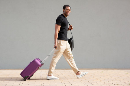 Man in casual clothing pulling a purple suitcase while walking on a tiled city sidewalkの写真素材