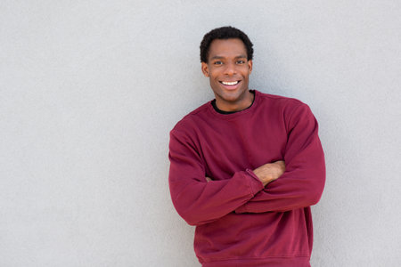 A man wearing a red sweater stands with his arms crossed, smiling confidently in front of a grey wallの写真素材