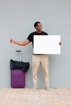 Man in casual clothing standing against a wall, holding a blank white sign and giving a thumbs upの写真素材